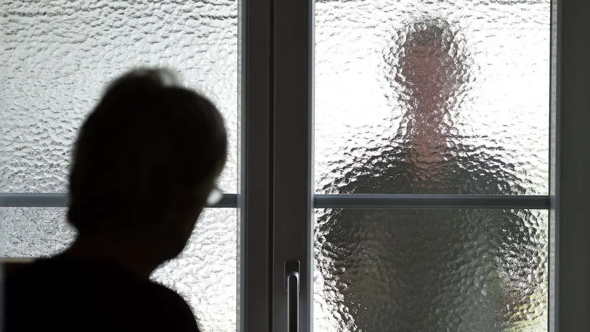 ARCHIV - ILLUSTRATION - Eine Frau steht am 05.07.2016 in Garmisch-Partenkirchen (Bayern) an einer Glasscheibe, hinter der ein Stalker steht. (gestellte Szene). (zu dpa «Verschärfung des Stalking-Paragrafen: Experten noch skeptisch» vom 11.12.2017) Foto: Jens Büttner/dpa-Zentralbild/dpa +++(c) dpa - Bildfunk+++