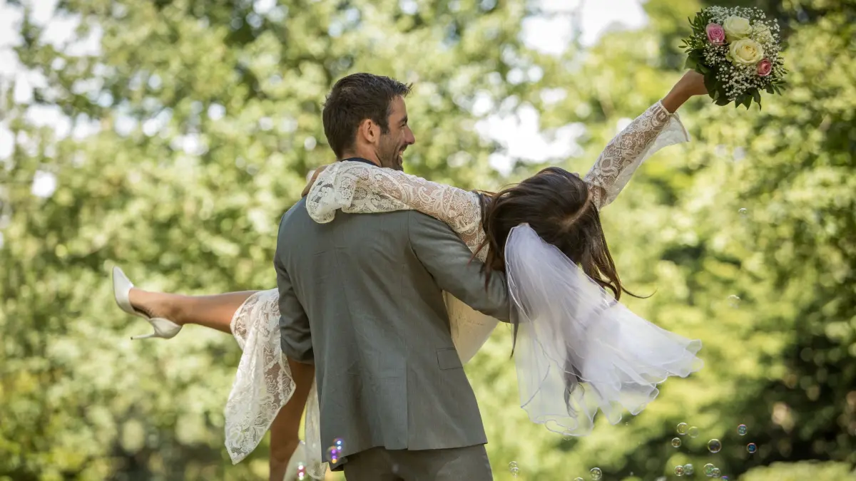 Ein Bräutigam trägt seine Braut: ILLUSTRATION - Die Freude ist groß, die Rechnung unter Umständen auch: Eine Hochzeit kann finanziell schnell ausufern. (zu dpa: «Hochzeit planen: Was die Feier wirklich kostet») Foto: Christin Klose/dpa-tmn - Honorarfrei nur für Bezieher des dpa-Themendienstes +++ dpa-Themendienst +++