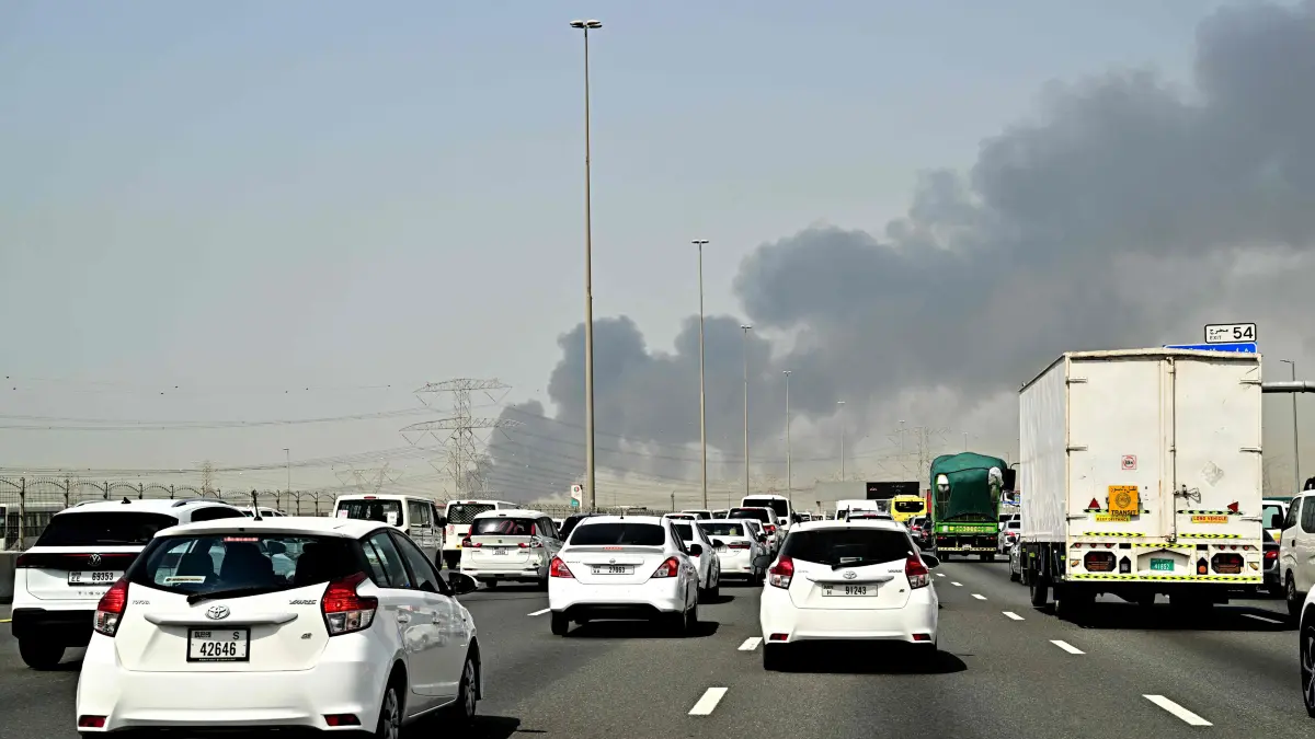 Smoke billows from an ongoing fire near Dubai International Airport as vehicles drive on a highway in Dubai on March 16, 2026. Flights were gradually resuming at Dubai airport on March 16, previously the world's busiest for international flights, the airport operator said, after a "drone-related incident" sparked a fuel tank fire nearby, as Iran kept up its Gulf attacks. (Photo by AFP) /
