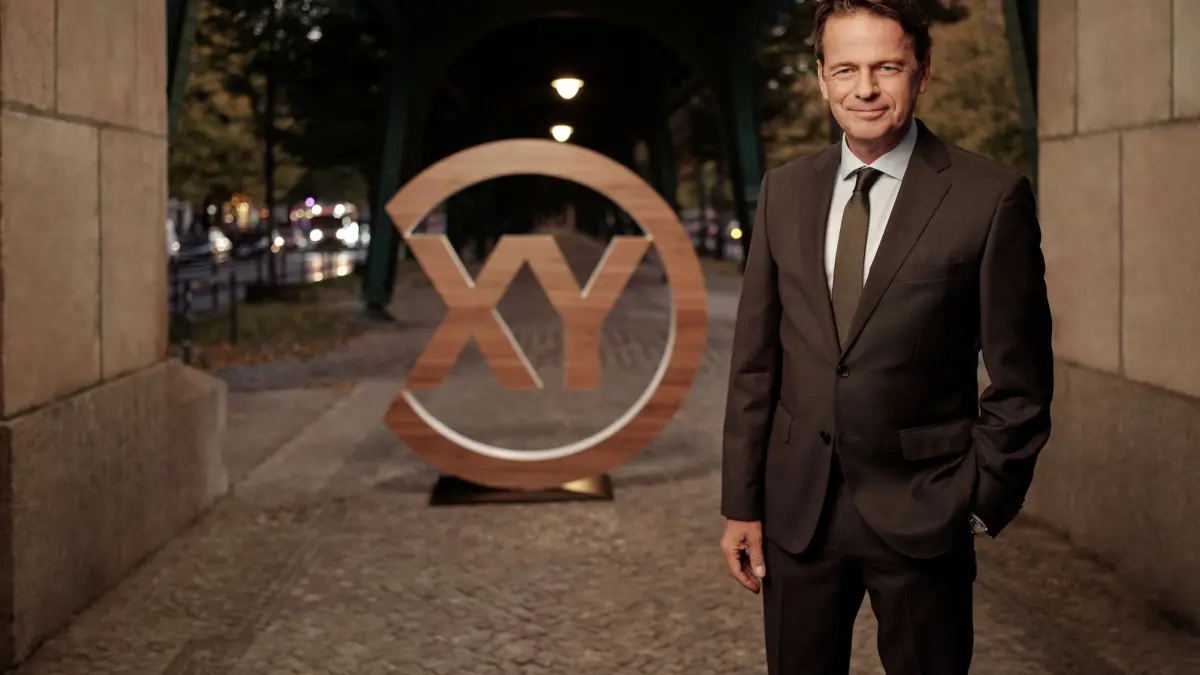 "Aktenzeichen XY… Ungelöst": Rudi Cerne steht vor dem "XY"-Logo und lächelt in die Kamera.