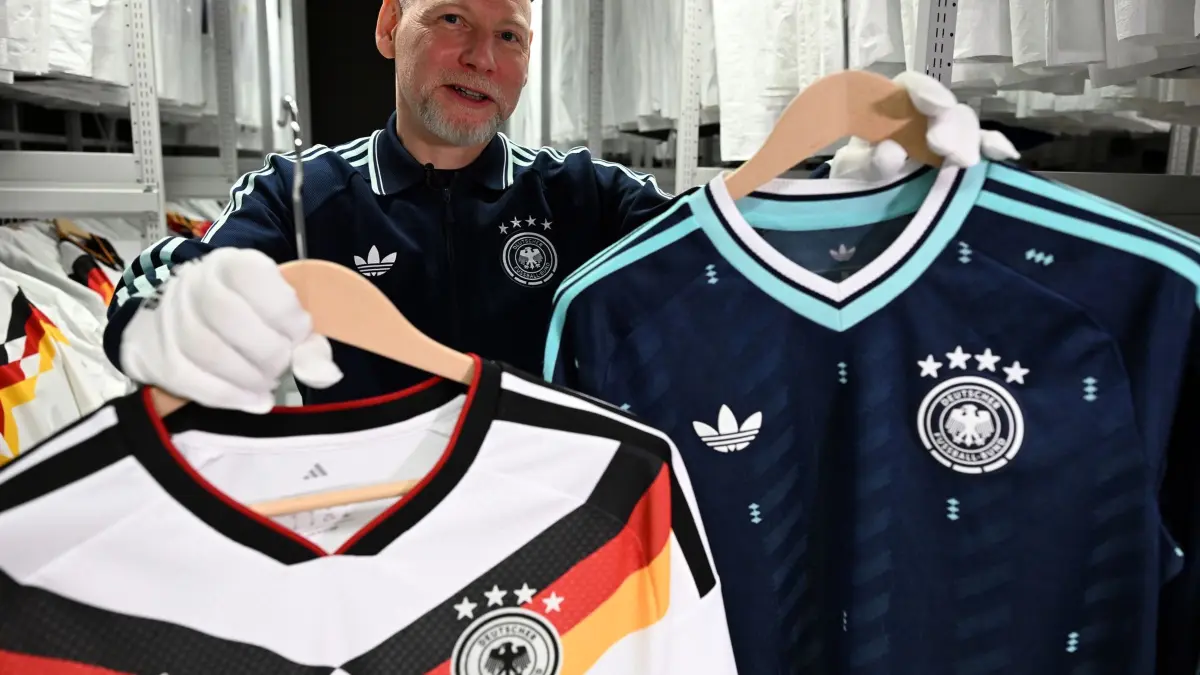 Adidas-Archiv: 25.03.2026, Bayern, Herzogenaurach: Designer Jürgen Rank hält Trikots der Nationalmannschaft in den Händen, die er gestaltet hat. Adidas zeigte Journalisten das Firmen-Archiv. Foto: Federico Gambarini/dpa - WICHTIGER HINWEIS: Gemäß den Vorgaben der DFL Deutsche Fußball Liga bzw. des DFB Deutscher Fußball-Bund ist es untersagt, in dem Stadion und/oder vom Spiel angefertigte Fotoaufnahmen in Form von Sequenzbildern und/oder videoähnlichen Fotostrecken zu verwerten bzw. verwerten zu lassen. +++ dpa-Bildfunk +++