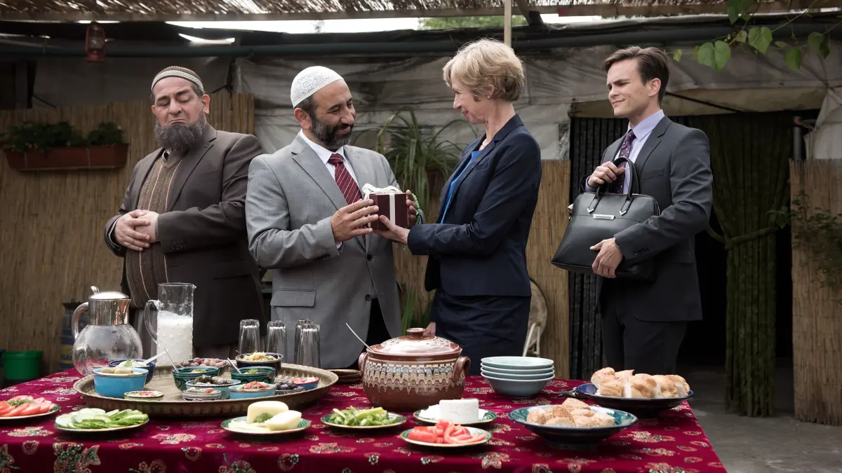 Beim Gegenbesuch auf dem Hof der alten Moschee bringen die Bürgermeisterin Ursel Piepenkötter (Anna Stieblich) und ihr Assistent Meyer (Eric Klotzsch, r.) Gastgeschenke für Osman (Hasan Ali Mete, l.) und Nuri Hodscha (Hilmi Sözer, 2.v.l.) mit,