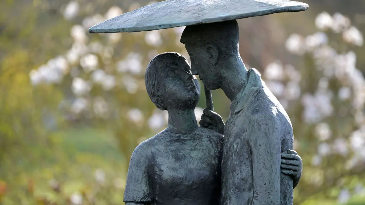 Wetter in Brandenburg: 05.04.2026, Brandenburg, Potsdam: Die Skulptur «Liebespaar mit Schirm» (Jürgen von Woyski, 1962,), Teil der Dauerausstellung «Plastik im Freien», steht vor Blüten einer Magnolie auf der Freundschaftsinsel. Foto: Michael Bahlo/dpa +++ dpa-Bildfunk +++