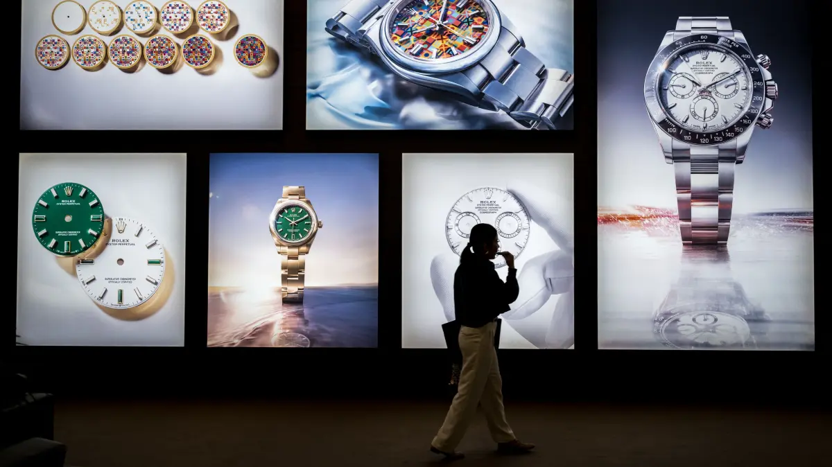 A visitor walks past photographs at the stand of Swiss luxury watchmaker Rolex during the opening day of the "Watches and Wonders Geneva" luxury watch fair, in Geneva, on April 14, 2026. The Geneva watch fair opened on April 14 and will be taken as a barometer of how the Middle East war is affecting the luxury goods sector. The Watches and Wonders salon -- the industry's biggest annual event -- sees 65 major watch brands, including Rolex, Patek Philippe, Cartier and Bulgari, display their latest creations until April 20. (Photo by Fabrice COFFRINI / AFP)