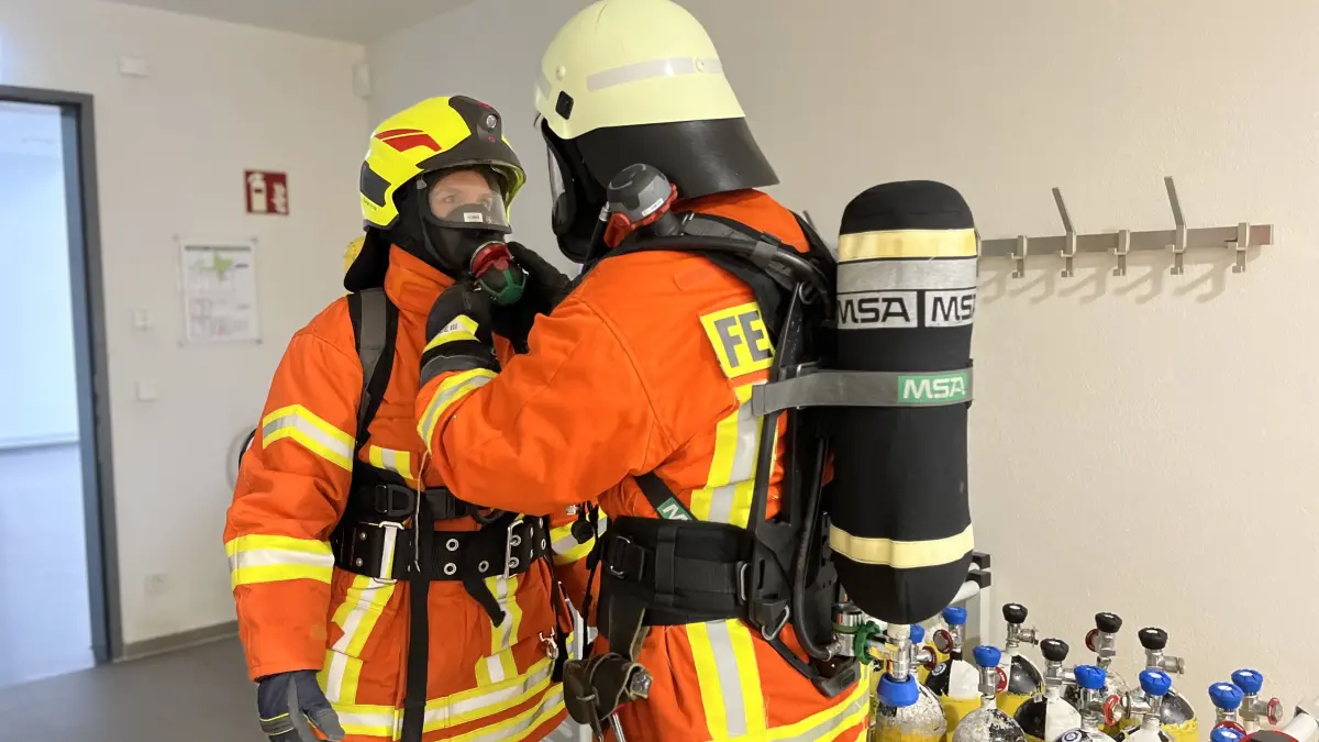 Die Feuerwehrleute helfen einander beim Richten der Maske.