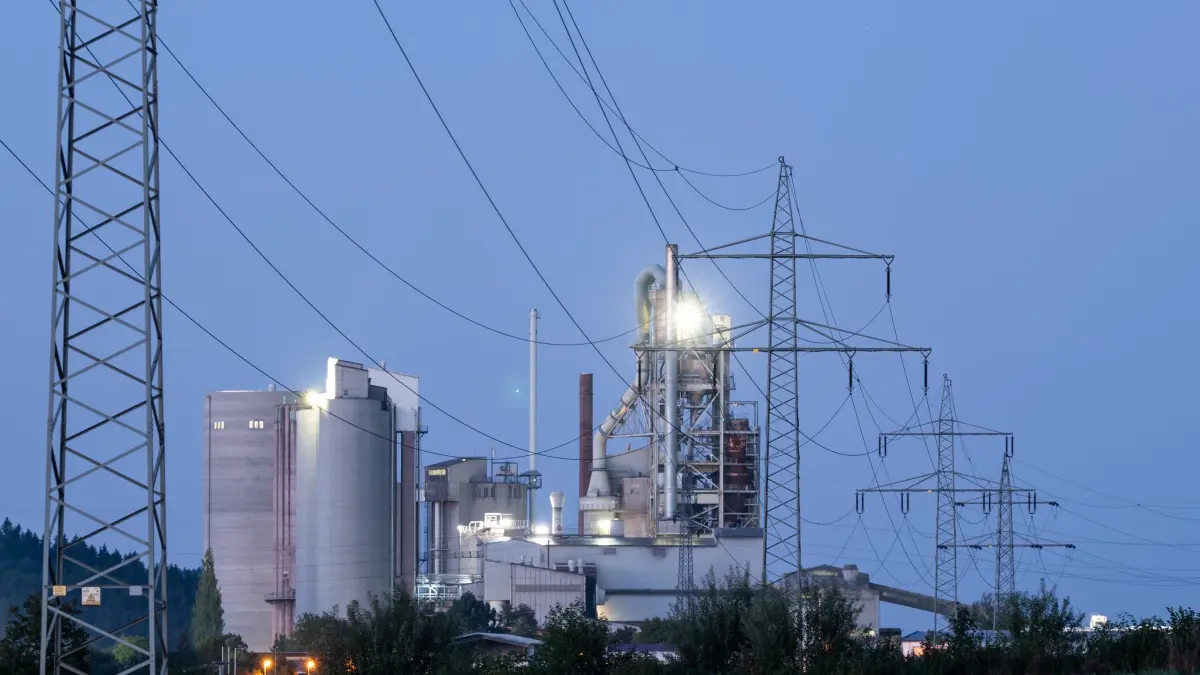 Industrie: ARCHIV - 06.09.2023, Baden-Württemberg, Rottweil: Strommasten stehen im Morgenlicht vor einem Zementwerk. (zu dpa: «Industrie erhält Milliardenhilfe für günstigeren Strom») Foto: Silas Stein/dpa +++ dpa-Bildfunk +++