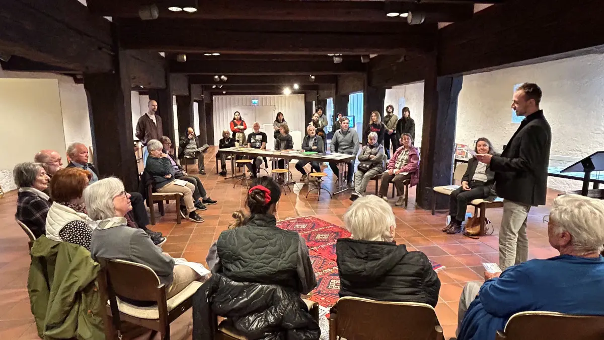 Vernissage in der Galerie im Alten Bau - Kurator des Projektes, David Quigley - Im erweiterten "Stuhlkreis" erläuterten bei der Vernissage die Ausstellungsmacher, hier Domenik Gebhardt vom Kunst- und Geschichtsverein, dass der Gestaltungsprozess jetzt erst begonnen hat. Denn die Wände der Galerie sind noch kahl.