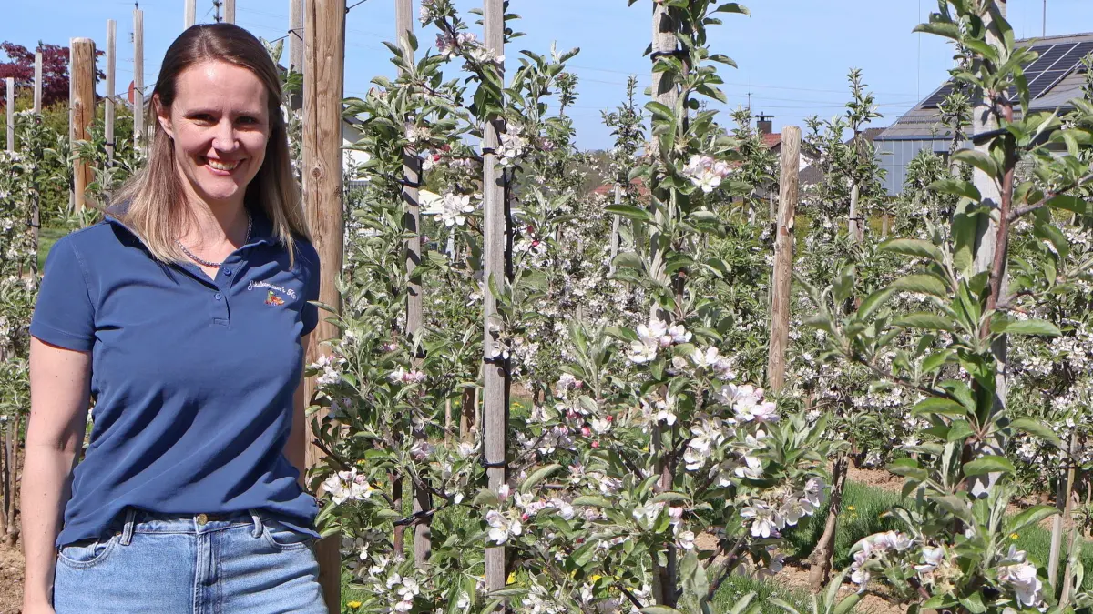 Meike Müller steht inmitten einer Apfelanlage in unmittelbarer Nähe des Hofes