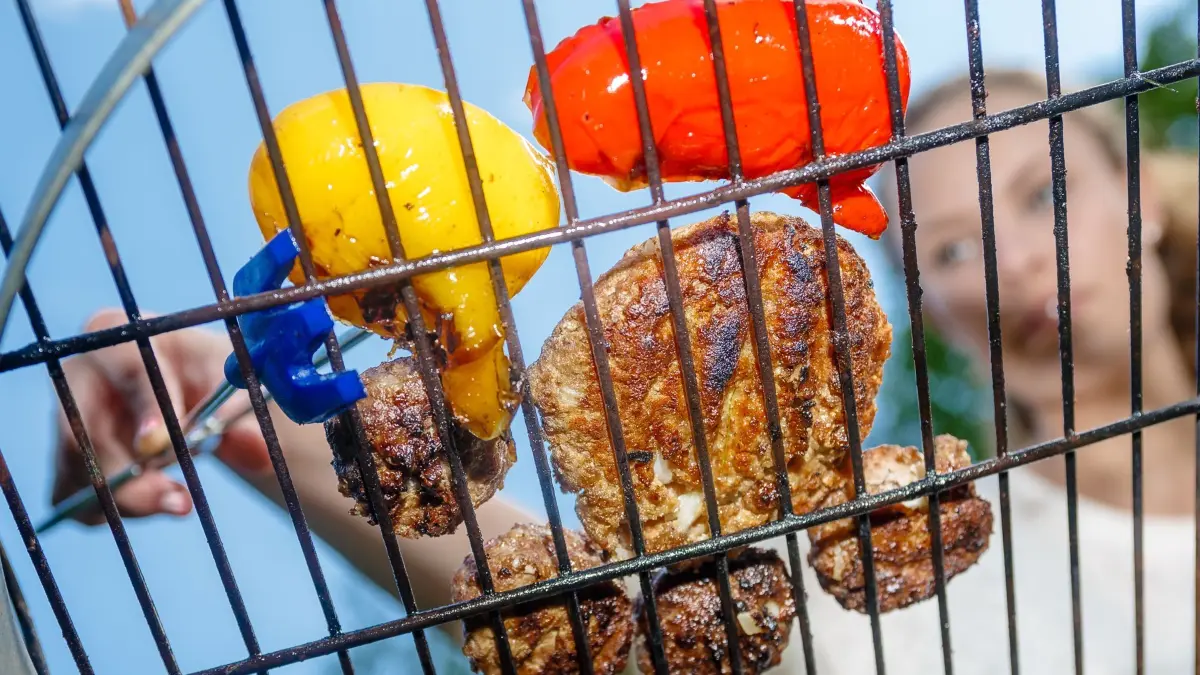 Frau grillt Fleisch und Paprika: ILLUSTRATION - Wer vor dem Grillen den Rost mit etwas Speiseöl bestreicht, hat es beim Putzen anschließend leichter. (zu dpa: «Mit Öl: So wird der Grillrost leichter sauber») Foto: Markus Scholz/dpa-tmn - Honorarfrei nur für Bezieher des dpa-Themendienstes +++ dpa-Themendienst +++