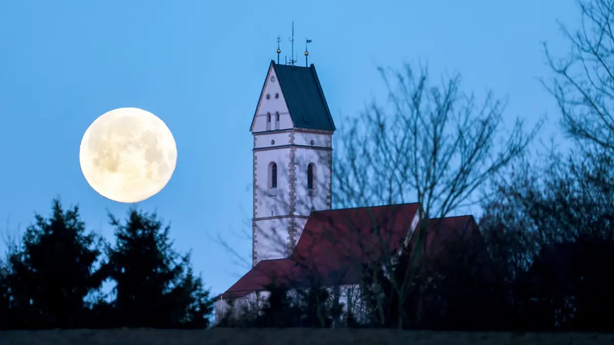 Vollmond: ARCHIV - 25.02.2024, Baden-Württemberg, Uttenweiler: Der Vollmond geht am Morgen kurz nach sonnenaufgang neben der Kirche St. Johannes Baptist in Offingen am Berg "Bussen" unter. (zu dpa: «Blue Moon im Mai über Südwesten - was es damit auf sich hat») Foto: Thomas Warnack/dpa +++ dpa-Bildfunk +++