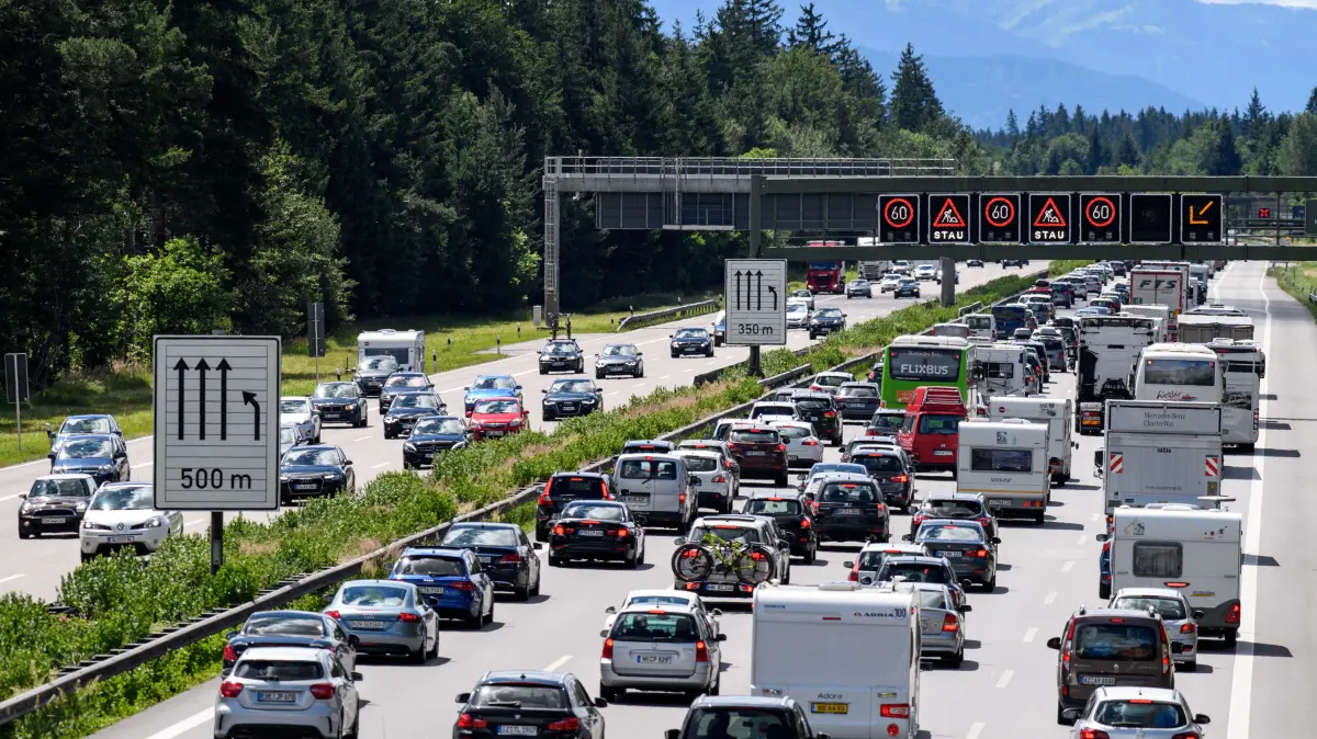 Dichter Verkehr schiebt sich am 01.07.2017 über die Autobahn 8 in Fahrtrichtung Salzburg und Brenner-Autobahn im Hofoldinger Forst bei Sauerlach (Bayern), während über der Straße auf einer digitalen Anzeige vor Stau gewarnt wird. Auf Bayerns Autobahnen staut sich der Verkehr an diesem Tag, da am Wochenende die Sommerferien in drei deutschen Bundesländern begonnen haben. Im Hintergrund sind die Alpen zu sehen. (zu dpa "Ferienbeginn in mehreren Bundesländern sorgt für Staus in Bayern" vom 01.07.2017) Foto: Matthias Balk/dpa ++ +++ dpa-Bildfunk +++
