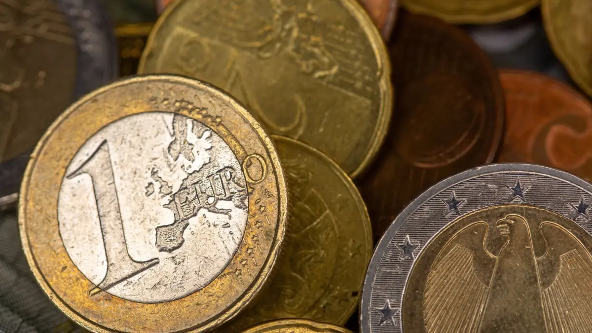 Münzen verschiedener Euro-Wertstufen liegen verstreut auf einem Tisch, darunter ein und zwei Euro- sowie Cent-Stücke. Im Hintergrund sind Teile von Euro-Banknoten zu sehen. (zu dpa: «Beschäftigte in Baden-Württemberg verdienen mehr Geld») +++ dpa-Bildfunk +++