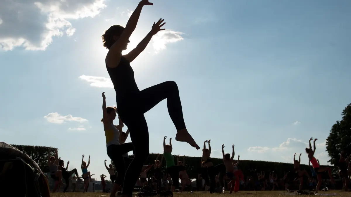 Sport im Park: ARCHIV - 26.07.2018, Sachsen, Dresden: Zahlreiche Teilnehmer stehen während eines Yoga-Kurses auf einer Wiese. (zu dpa: «Von Aerobic bis Zumba - Was «Sport im Park» zu bieten hat») Foto: Sebastian Kahnert/dpa +++ dpa-Bildfunk +++