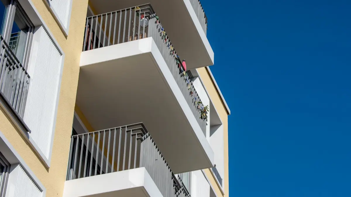 Blick von unten auf Balkons eines Mehrfamilienhauses: ILLUSTRATION - Balkon im Sicherheitscheck: Kisten, Stühle und Tische weg von der Brüstung, damit Kinder nicht hochklettern können. (zu dpa: «Mit Kleinkindern keine Getränkekisten auf den Balkon stellen») Foto: Zacharie Scheurer/dpa-tmn - Honorarfrei nur für Bezieher des dpa-Themendienstes +++ dpa-Themendienst +++