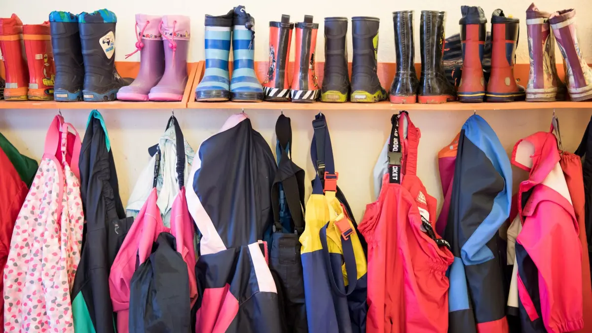 Kindergarten: ARCHIV - 05.02.2018, Schleswig-Holstein, ---: SYMBOLBILD - 05.02.2018, Schleswig-Holstein: Gummistiefel und Regenhosen von Kindern hängen an einem Regal. (zu dpa: «Weniger Kinder, höhere Kosten: Bericht zur Kita-Finanzierung») Foto: Christian Charisius/dpa +++ dpa-Bildfunk +++