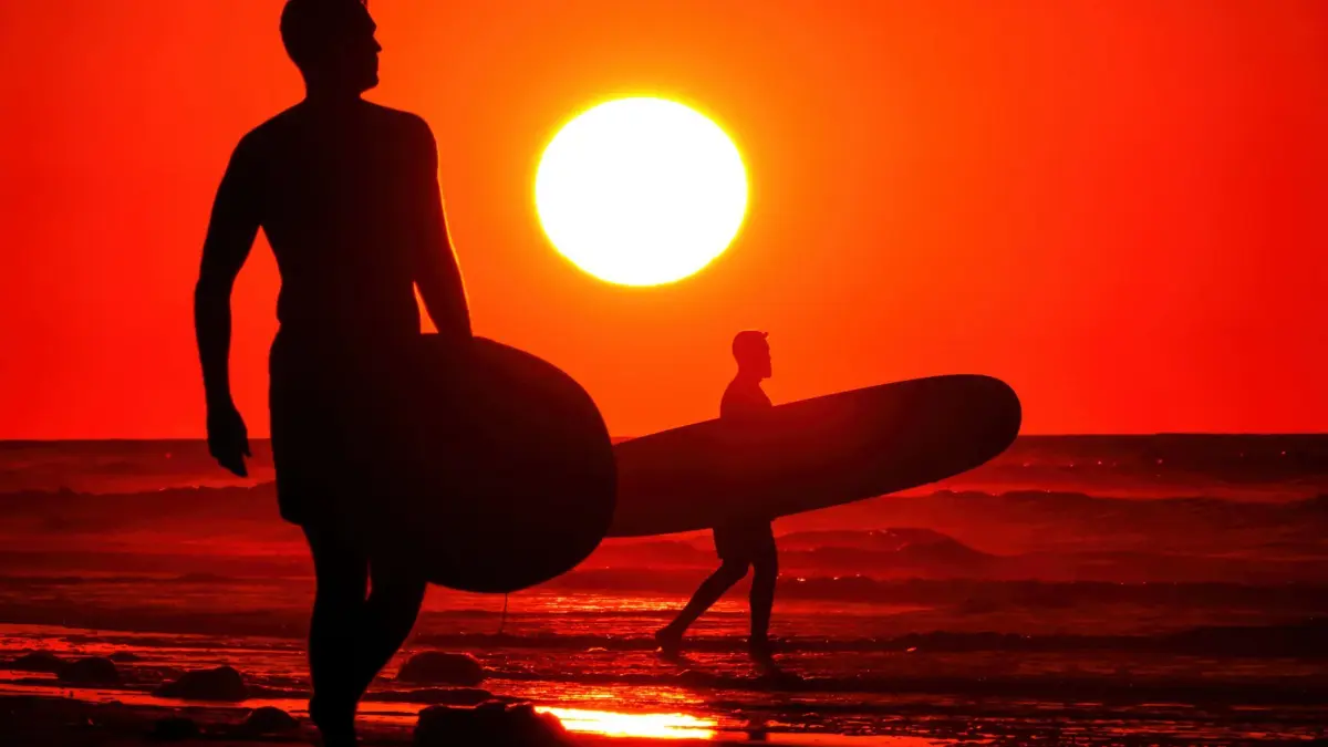 Sonnenaufgang über Folly Beach in South Carolina: 16.05.2026, USA, Folly Strand: Surfer, deren Silhouetten sich im Sonnenaufgang abzeichnen, gehen den Strand entlang auf der Suche nach der perfekten Welle. Foto: Richard Ellis/ZUMA Press Wire/dpa +++ dpa-Bildfunk +++