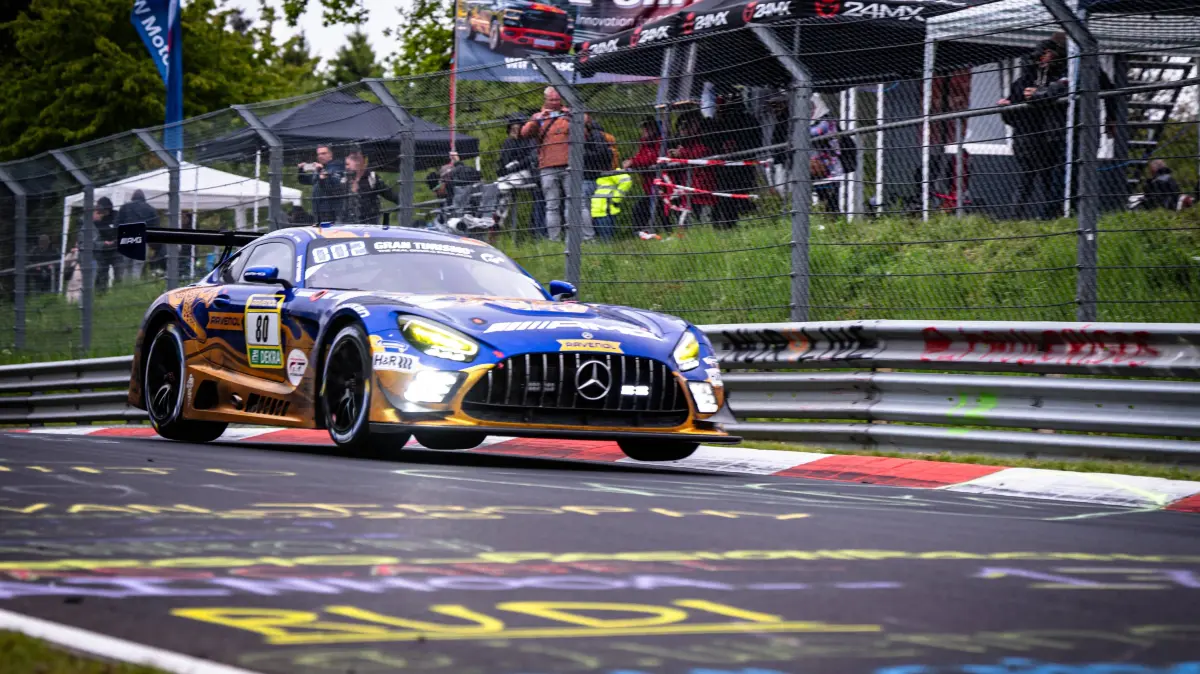 Mercedes-AMG GT3 #80 von RAVENOL auf der Nordschleife: Der Mercedes-AMG GT3 80 von Mercedes-AMG Team RAVENOL durchfährt mit eingeschalteten Scheinwerfern eine Kurve auf der Nordschleife des Nürburgrings. Das Fahrzeug trägt das charakteristische blau-goldene Livery mit RAVENOL- und H&R-Sponsoring und ist im typischen Gran Turismo-Design lackiert. Im Hintergrund verfolgen zahlreiche Zuschauer hinter dem Fangzaun das Renngeschehen. Fabian Schiller & Luca Stolz & Maro Engel & Maxime Martin Mercedes-AMG Team RAVENOL Mercedes-AMG GT3 80 von RAVENOL auf der Nordschleife *** The Mercedes AMG GT3 80 from Mercedes AMG Team RAVENOL drives through a corner on the Nordschleife of the Nürburgring with its headlights switched on The vehicle wears the characteristic blue and gold livery with RAVENOL and H R sponsorship and is painted in the typical Gran Turismo design In the background, numerous spectators watch the race behind the catch fence Fabian Schiller Luca Stolz Maro Engel Maxime Martin Mercedes AMG Team RAVENOL Mercedes AMG GT3 80 from RAVENOL on the Nordschleife Copyright: xMichaelxGelhardtx