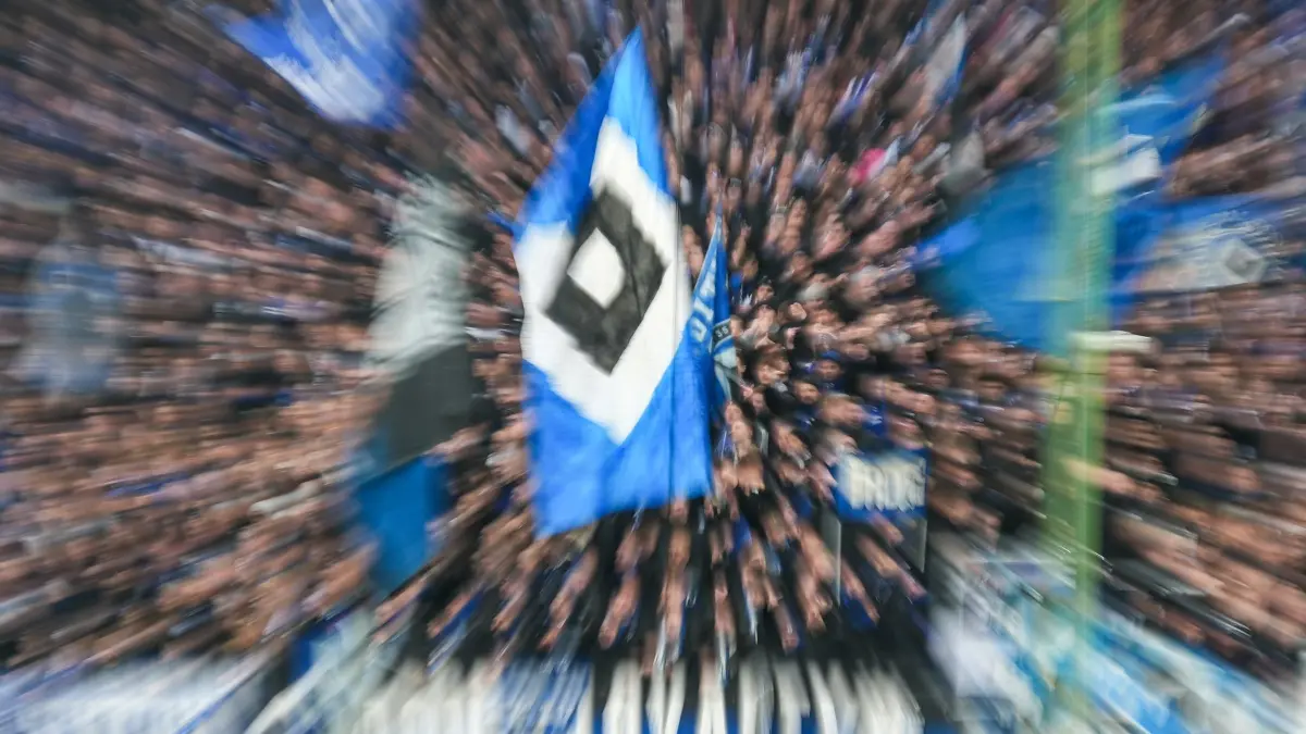 HSV-Frauen: ARCHIV - 07.12.2025, Hamburg: Fußball: Bundesliga, Hamburger SV - SV Werder Bremen, 13. Spieltag, Volksparkstadion. HSV-Fahne vor dem Spiel im Hamburger Fanblock (Aufnahme mit Zoom-Effekt). WICHTIGER HINWEIS: Gemäß den Vorgaben der DFL Deutsche Fußball Liga bzw. des DFB Deutscher Fußball-Bund ist es untersagt, in dem Stadion und/oder vom Spiel angefertigte Fotoaufnahmen in Form von Sequenzbildern und/oder videoähnlichen Fotostrecken zu verwerten bzw. verwerten zu lassen. Die Fußballerinnen des Hamburger SV haben den Klassenverbleib geschafft. (zu dpa: «Wie die Männer: HSV-Frauen schaffen Klassenerhalt») Foto: Marcus Brandt/dpa +++ dpa-Bildfunk +++