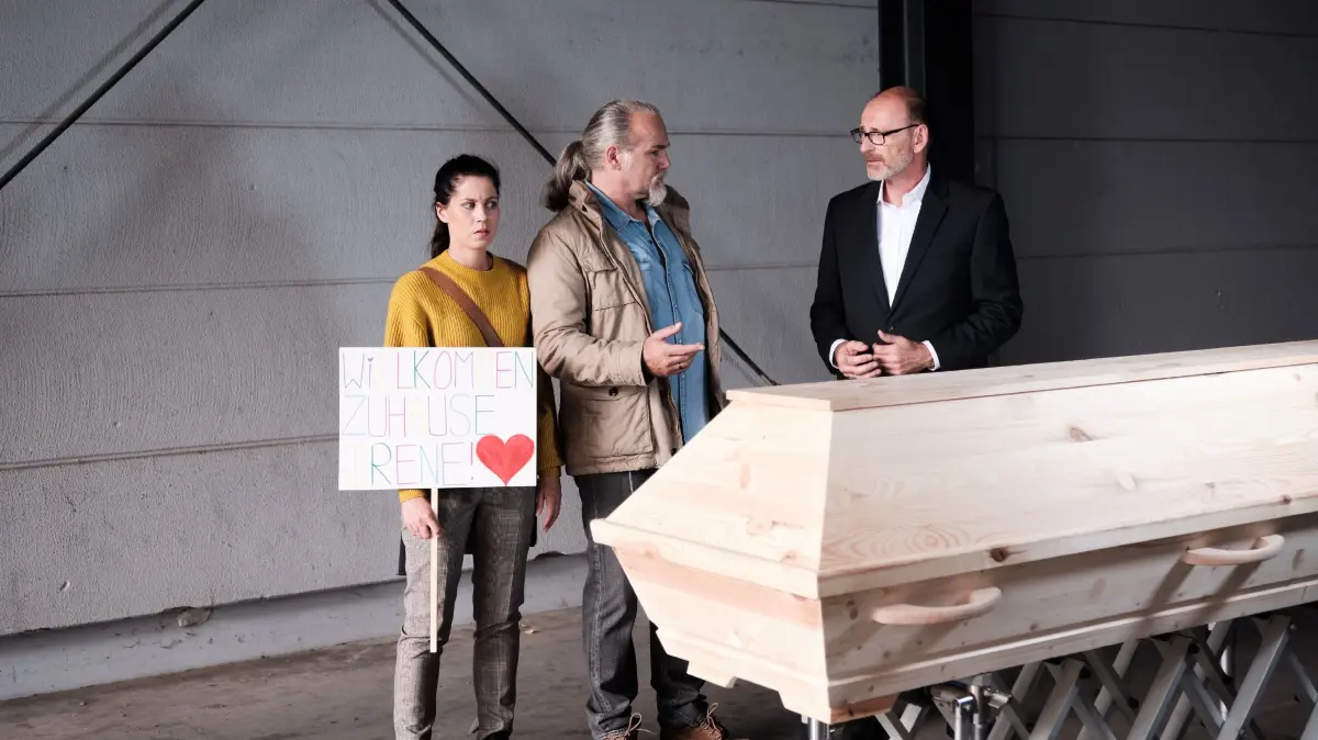2019: Sina (Valea Scalabrino) und Robert (Luca Maric, M.) nehmen schockiert Irene in Empfang: in einem Sarg. Rechts Werner Scholz (Frank Weber)