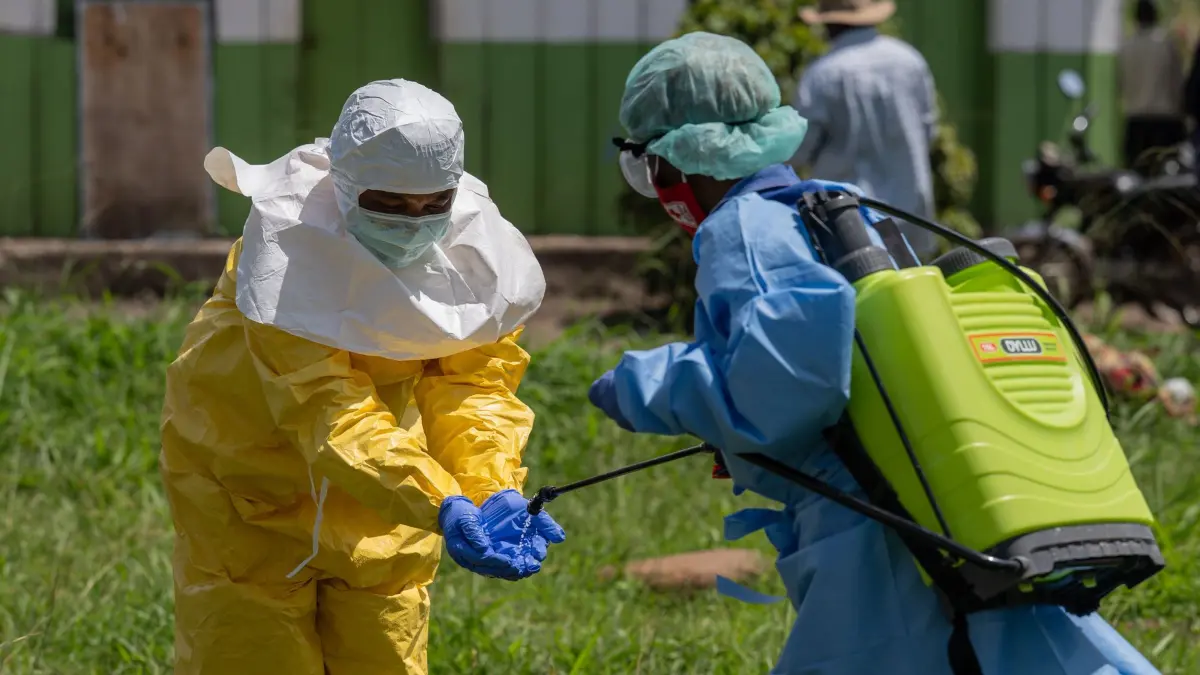 Ebola-Ausbruch - Kongo: ARCHIV - 20.05.2026, Demokratische Republik Kongo, Rwampara: Ein Mitarbeiter des Roten Kreuzes (l) wird desinfiziert, nachdem er die Leichen von Menschen, die an Ebola gestorben sind, aus einem Gesundheitszentrum in Rwampara abtransportiert hat. (zu dpa: «Schweißtreibender Einsatz im Schutzanzug») Foto: Moses Sawasawa/AP/dpa +++ dpa-Bildfunk +++
