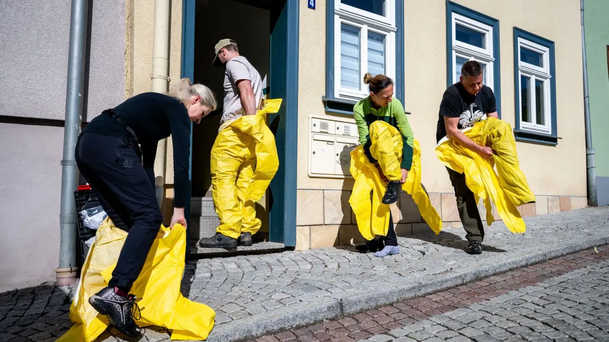 Tatortreiniger im Thüringer Wald im Einsatz: PRODUKTION - 19.05.2026, Thüringen, Ilmenau: Firmeninhaberin Bernadeta Lotze (47, l), Kevin Lotze (24, 2.v.l.), Bozena Mazurkiewicz (2.v.r.) und Jan Mazurkiewicz (r) ziehen ihre Schutzanzüge an, bevor sie mit der Wohnungsreinigung im Thüringer Wald am 19. Mai 2026 beginnen. In der Wohnung wurde die verstorbene Bewohnerin aufgefunden. Die Firma Tatortreinigung Lotze führt die Reinigung von Tatorten, Unfallorten sowie stark kontaminierten Räumlichkeiten durch. (zu dpa: «Letzte Spuren - vom Alltag einer Tatortreinigerin») Foto: Jacob Schröter/dpa +++ dpa-Bildfunk +++