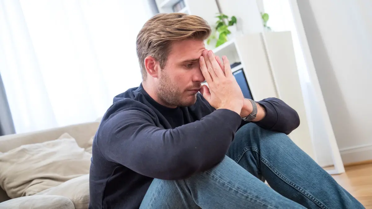 Ein junger Mann gestresst in einem Wohnzimmer: ILLUSTRATION - Überfordert von ungewohnten Situationen? Mini-Schritte statt Rückzug: Veränderungen dosiert üben und stabile Routinen behalten – so lässt sich der Kreislauf durchbrechen. (zu dpa: «Neue Situationen überfordern? So lassen sich Ängste abbauen») Foto: Christin Klose/dpa-mag - Honorarfrei nur für Bezieher des Dienstes dpa-Magazin +++ dpa-Magazin +++