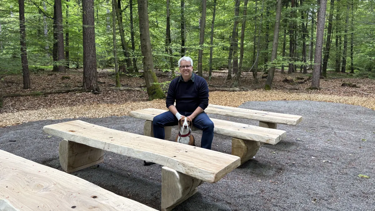 Roland Hartz, Forstbezirksleiter ForstBW sitzt am Versammlungsplatz des Friedwaldes auf einer Holzbank aus heimischer Eiche.