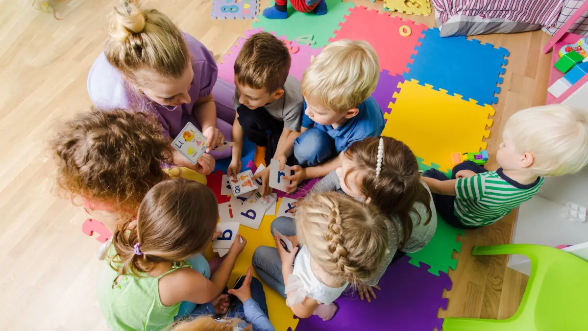 Group of kindergarten kids sitting closely on a floor together with teacher, providing group work. Children learning to cooperate while solving tasks.