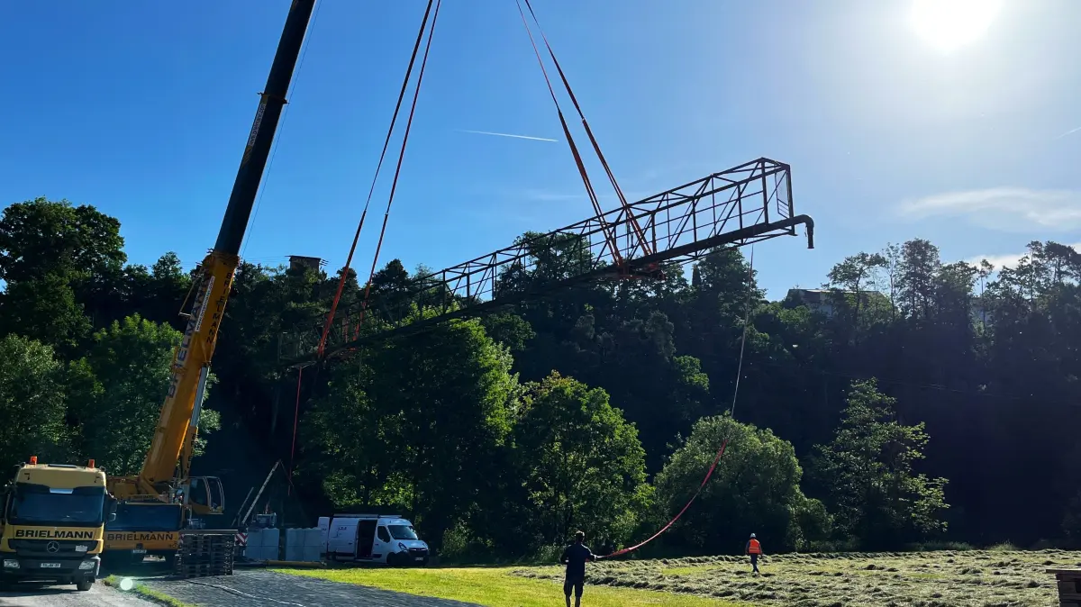 Die Leitungsbrücke über den Neckar bei Fischingen schwebt. Um sie zu sanieren, wird sie mithilfe eines Autokrans angehoben und neben das Sportgelände platziert.
