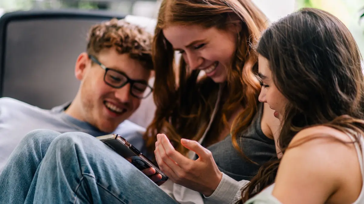 Freunde blicken lachend auf ein Smartphone: ILLUSTRATION - In einem Moment traurig im nächsten wieder hoffnungsvoll: Gefühle können sich schnell wieder ändern. Heißt also: Ertappen wir uns dabei, etwas Schönes nicht zu genießen, ist es in vielen Fällen noch zu retten. (zu dpa: «Urlaub und Co.: Was, wenn ich Schönes nicht genießen kann?») Foto: Zacharie Scheurer/dpa-tmn - Honorarfrei nur für Bezieher des dpa-Themendienstes +++ dpa-Themendienst +++