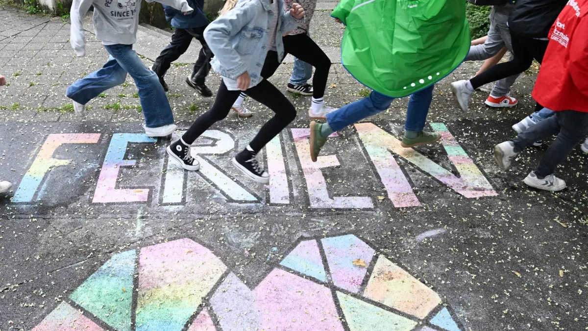 Ferienbeginn: ARCHIV - 30.07.2025, Baden-Württemberg, Stuttgart: Schüler einer Grundschule laufen am letzten Schultag vor den Sommerferien in Baden-Württemberg über einen bunten Kreide-Schriftzug «Ferien». (zu dpa: «Lehrer fordern: Sommerferien nicht vor Anfang Juli») Foto: Bernd Weißbrod/dpa +++ dpa-Bildfunk +++