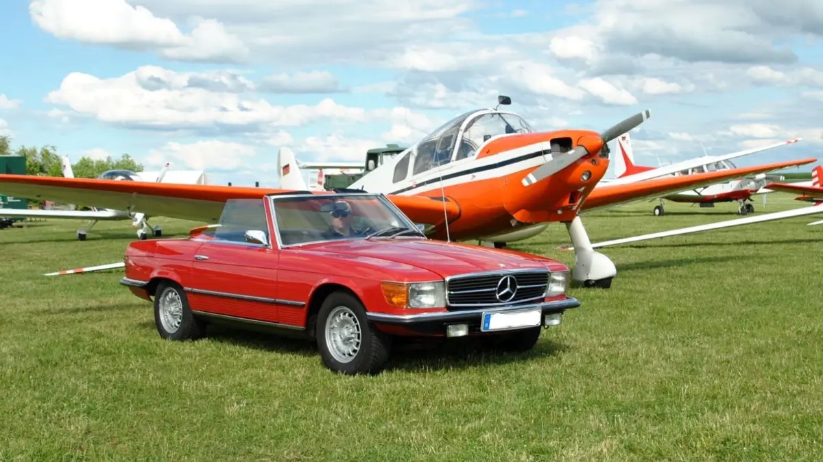 Stolz auf sein Traumauto: OFE-Mitgründer Uwe Fischer mit seinem roten Mercedes Benz 350 SL (R107) vor historischer Kulisse auf dem Eutinger Fluggelände.