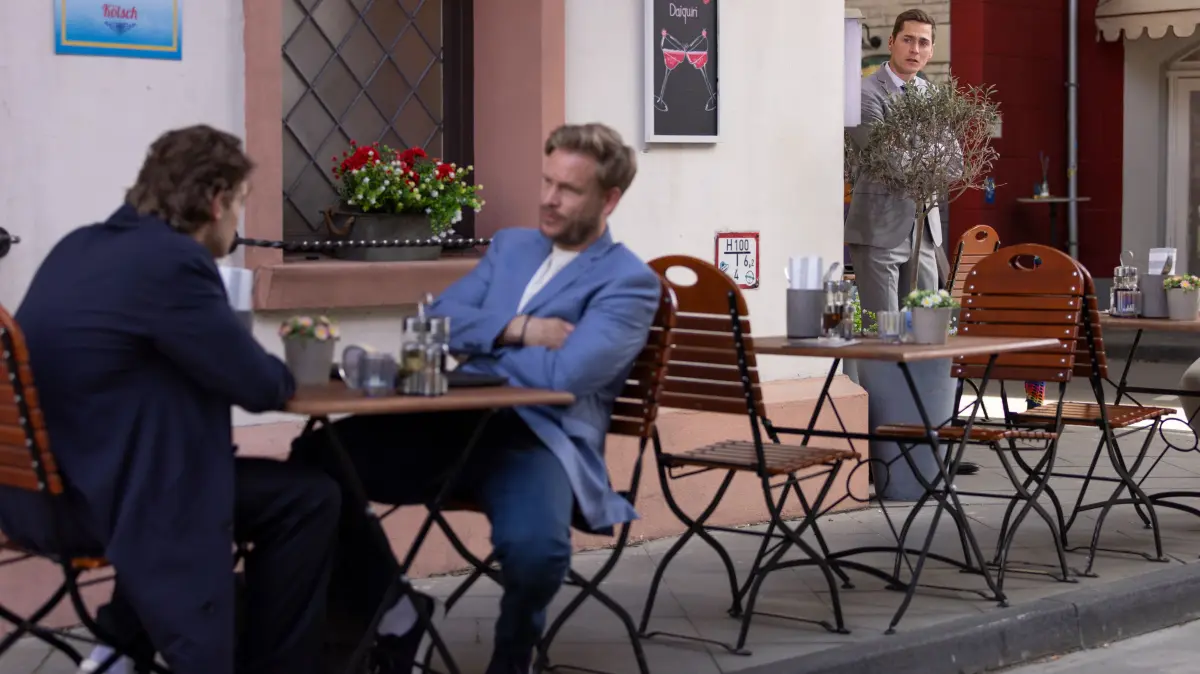 Ringo (Timothy Boldt, r.) kriegt entsetzt mit, dass Julius fortan alleinverantwortlich für Alexanders (Frederic Heidorn, M.) krumme Coaching-Geschäfte sein wird.