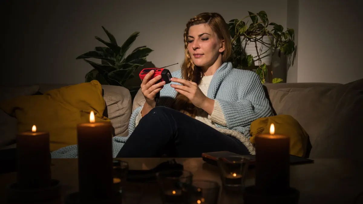Eine Frau mit Kerzen während eines Stromausfalls auf dem Sofa: ILLUSTRATION - Blackout? Taschenlampe, Kerzen und Kurbelradio sorgen für Licht und Nachrichten auch ohne Netz. (zu dpa: «Licht und Co.: Was Sie bei Stromausfällen wirklich brauchen») Foto: Christin Klose/dpa Themendienst/dpa-tmn - Honorarfrei nur für Bezieher des dpa-Themendienstes +++ dpa-Themendienst +++