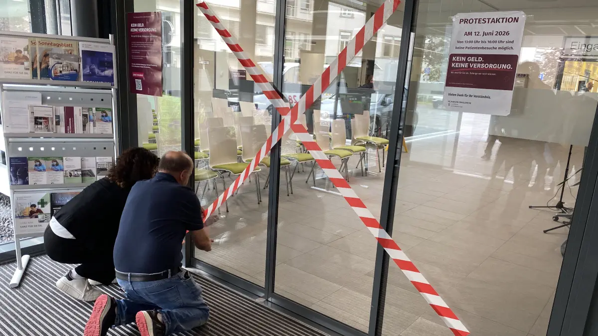 Symbolisch bleiben die Türen des Klinikums Crailsheim für drei Stunden geschlossen. Anja Dreher, Stabstelle Kommunikation, und Friedemann Spengler, stellvertretender Technischer Leiter, kleben Absperrband vor die Eingangstür.