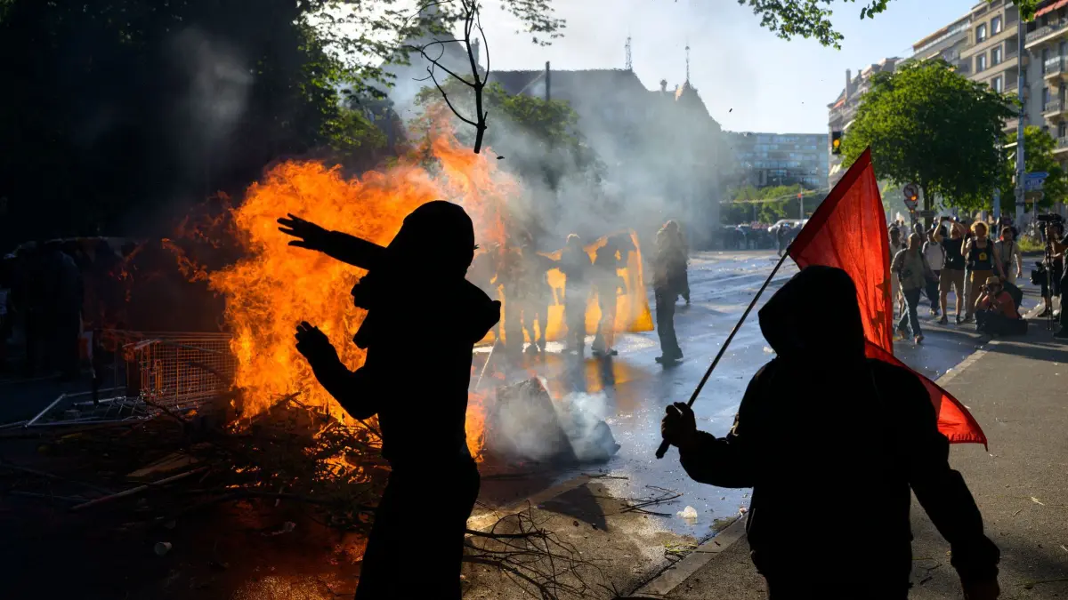 G7 Demonstrationen: 14.06.2026, Schweiz, Genf: "No-G7"-Aktivisten neben einem Feuer mitten auf der Straße während einer Demonstration gegen den G7-Gipfel, der vom 15. bis 17. Juni in Evian stattfinden soll. Foto: Jean-Christophe Bott/KEYSTONE/dpa +++ dpa-Bildfunk +++