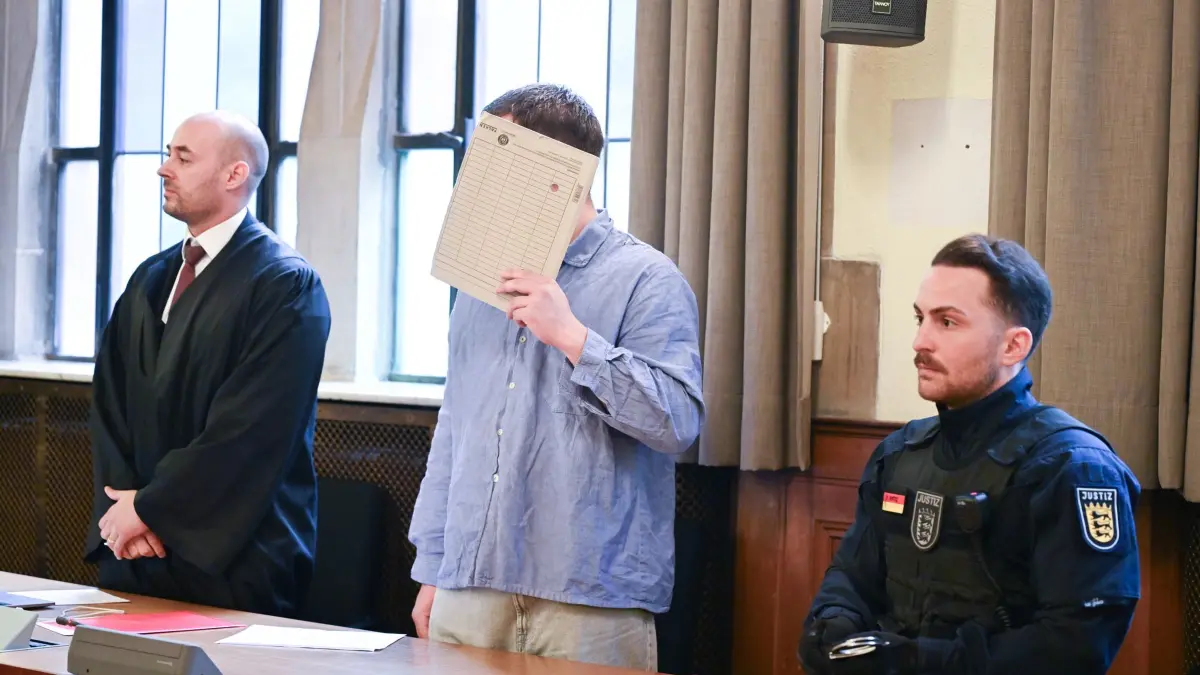 Prozess wegen versuchten Mordes: ARCHIV - 07.05.2026, Baden-Württemberg, Tübingen: Ein Angeklagter steht vor dem Beginn seines Prozesses wegen versuchten Mordes mit einem Aktendeckel vor dem Gesicht im Gerichtssaal. Links sein Anwalt Sebastian Gauss. Der Angeklagte soll im Oktober 2025 in die Wohnung seiner schlafenden Nachbarin in Tübingen eingedrungen sein und versucht haben, diese zu ersticken. (zu dpa: «Urteil nach Attacke auf schlafende Nachbarin erwartet») Foto: Bernd Weißbrod/dpa +++ dpa-Bildfunk +++