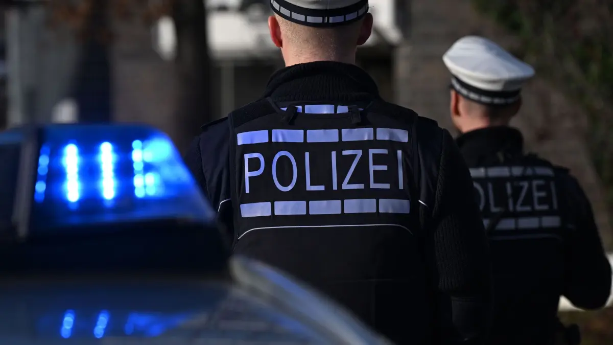 ARCHIV - 03.12.2024, Baden-Württemberg, Stuttgart: Das Logo der Polizei auf der Dienstkleidung von Polizisten die vor einem Blaulicht stehen (gestellte Szene). (zu dpa: «Mann stößt Lokführer auf Gleise und schlägt Polizisten») Foto: Bernd Weißbrod/dpa +++ dpa-Bildfunk +++