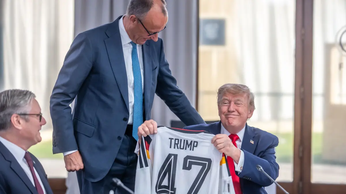 G7-Gipfel: 16.06.2026, Frankreich, Evian: Bundeskanzler Friedrich Merz (M, CDU) schenkt ein DFB Fußball Trikot an US-Präsident Donald Trump (r) mit der Rückennummer 47 vor der Arbeitssitzung zu den Themen Welthandel, Iran- und Ukraine-Krieg beim G7 Treffen in Evian während Keir Starmer, Premierminister von Großbritannien, daneben sitzt. Foto: Michael Kappeler/dpa-Pool/dpa +++ dpa-Bildfunk +++