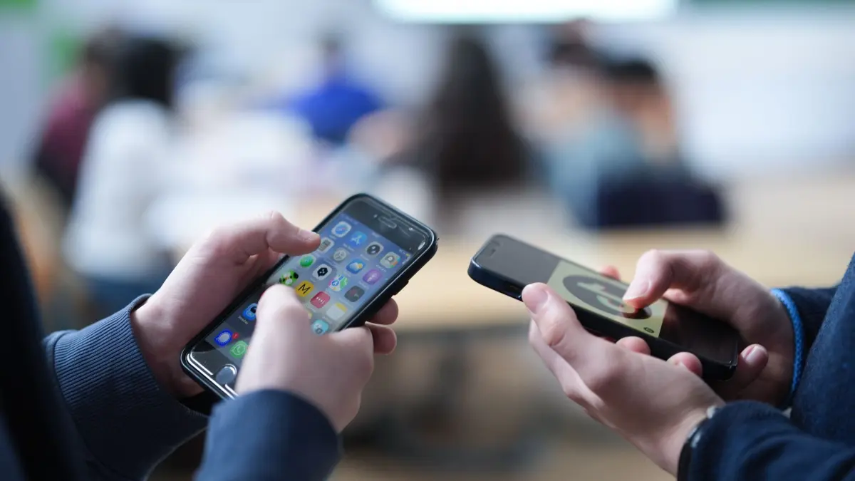 Smartphones in der Schule: ILLUSTRATION - 13.02.2026, Hamburg: Zwei Schüler stehen ein einem Klassenraum und schauen auf ihre Smartphones, auf einem der Displays ist das Logo der Social-Media-Plattform TikTok zu sehen. (zu dpa: «Polizei warnt nach Würge-Vorfall vor «Blackout Challenge»») Foto: Marcus Brandt/dpa +++ dpa-Bildfunk +++