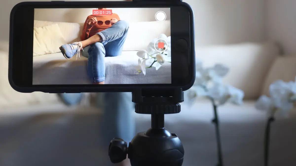 Influencing: ARCHIV - 08.03.2023, Bayern, Kaufbeuren: Eine Frau sitzt mit einer Sonnenbrille in Händen auf einem Sofa und filmt sich dabei mit ihrem iPhone (gestellte Szene). Produkttipps auf Instagram oder TikTok sind oft bezahlte Werbung. (zu dpa: «Ministerium: Influencer manchmal unsicher bei Besteuerung») Foto: Karl-Josef Hildenbrand/dpa +++ dpa-Bildfunk +++