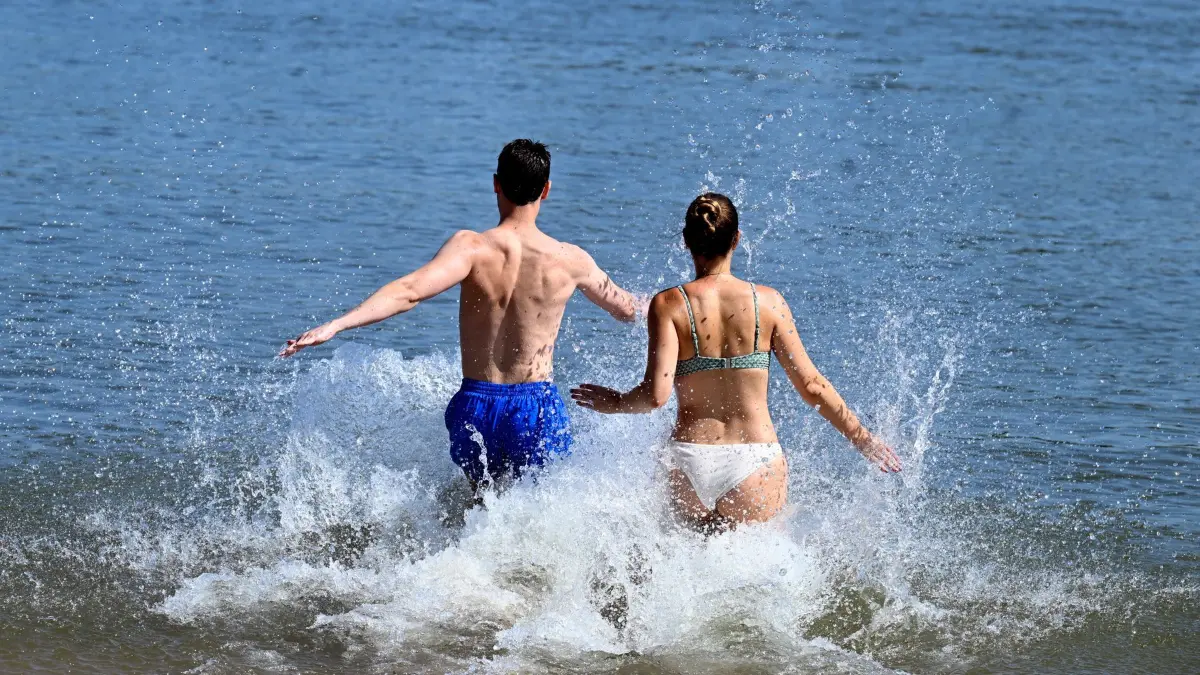 Sommerwetter in Nordrhein-Westfalen: ARCHIV - 20.07.2024, Nordrhein-Westfalen, Rodenkirchen: Ein Mann und eine Frau laufen in das kühle Wasser des Rheins. Vielerorts suchen die Menschen nach Abkühlung. (zu dpa: «Sonne brütet über NRW – am Sonntag drohen heftige Gewitter») Foto: Roberto Pfeil/dpa +++ dpa-Bildfunk +++