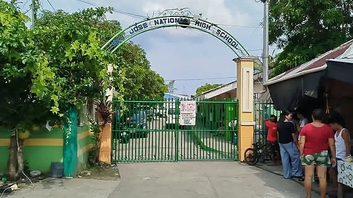 PHILIPPINES-SHOOTING-SCHOOL-CRIME: People stand next to the entrance gate of San Jose National High School after a shooting incident in Tacloban City, Leyte province on June 22, 2026. At least three teenaged students were killed and five others wounded on June 22, in a rare school shooting in the central Philippines, police said. (Photo by Noel Sianosa / AFP)