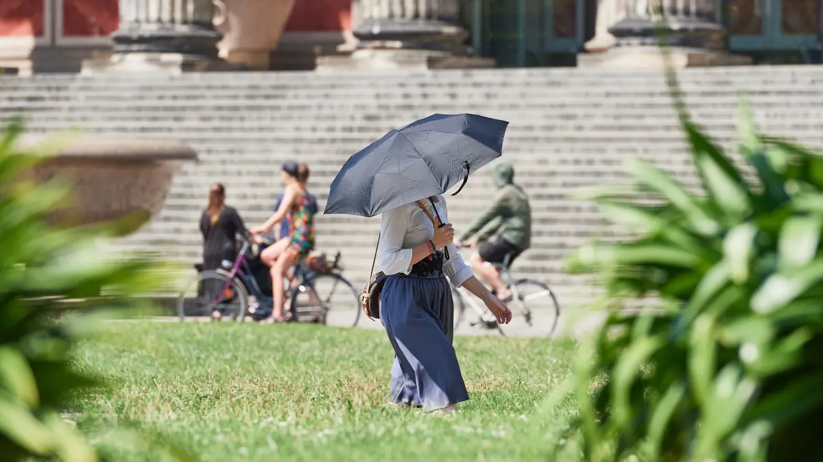 Strahlenschuetzer geben Tipps zum Umgang mit UV-Strahlung: Eine Frau schuetzt sich im Lustgarten in Berlin-Mitte mit einem Regenschirm vor den Sonnenstrahlen (Themenfoto vom 19.07.2022). Sommerzeit, die Sonne lacht, die Laune steigt - aber auch das Risiko. Unsichtbare UV-Strahlung ist nicht nur fuer Sonnenbraende verantwortlich, sondern auch fuer jaehrlich rund 350.000 neue Hautkrebsfaelle in Deutschland. Damit es nicht so weit kommt, laesst sich die Gefahr mit wenigen einfachen Massnahmen zum Sonnenschutz effektiv mildern. Die Experten des Bundesamtes fuer Strahlenschutz erlaeutern, was UV-Strahlung ist, was sie schlimmstenfalls anrichten kann - und wie man ihr wirksam begegnet. (Siehe epd-Bericht vom 23.06.2026) *** Local Caption *** 00471098