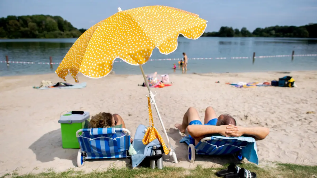 Wasserqualität der Badeseen: ARCHIV - 29.08.2024, Niedersachsen, Oldenburg: Ein Paar sitzt bei sonnigem Wetter und hohen Temperaturen auf zwei Liegen unter einem Sonnenschirm im Sand. (zu dpa: «Bis zu 38 Grad – Hitzewelle rollt auf Niedersachsen zu») Foto: Hauke-Christian Dittrich/dpa +++ dpa-Bildfunk +++