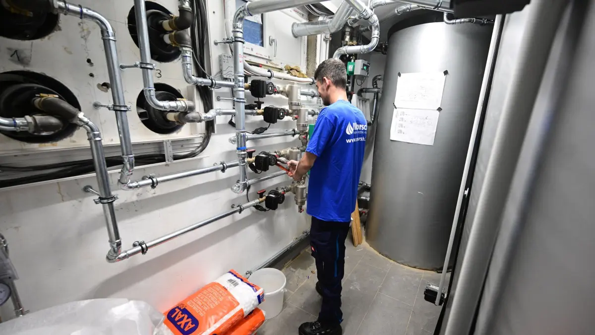Handwerker arbeitet an Installation der Technik einer Wärmepumpe: ARCHIV - Alle Fördermittel für den Umstieg auf eine klimafreundliche Heizung abzugreifen, kann für eine WEG durchaus kompliziert sein. Die einzelnen Haushalte haben separate Möglichkeiten. (zu dpa: «Heizungstausch in WEG: So sichern Sie sich alle Fördergelder») Foto: Bernd Weißbrod/dpa/dpa-mag - Honorarfrei nur für Bezieher des Dienstes dpa-Magazin +++ dpa-Magazin +++