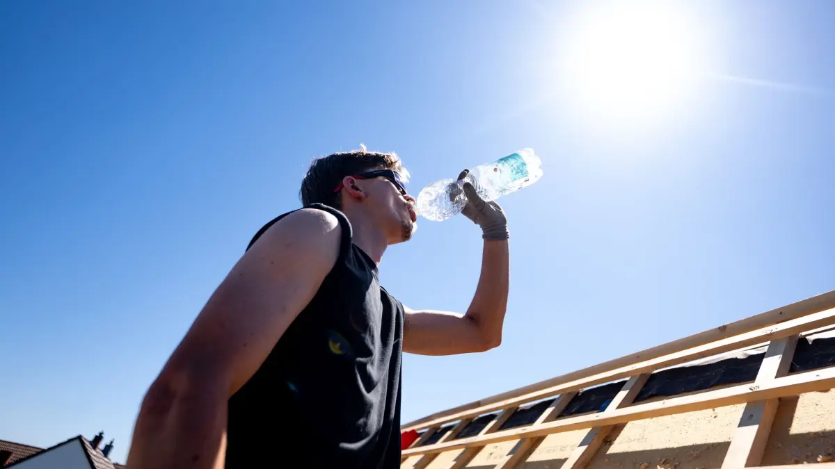 Wetter in Nordrhein-Westfalen: ARCHIV - 26.05.2026, Nordrhein-Westfalen, Sankt Augustin: Ein Dachdecker der Firma «Dachdecker Ditscheid» trinkt Wasser unter der sengenden Sonne bei über 30 Grad auf dem Dach eines Hauses im Rhein-Sieg-Kreis.
Alle 20 Minuten sollte man etwas trinken, wenn man sich in der Hitze viel bewegt. (zu dpa: «Kreislaufprobleme und mehr durch Hitze - Was Ärzte empfehlen») Foto: Benjamin Westhoff/dpa +++ dpa-Bildfunk +++