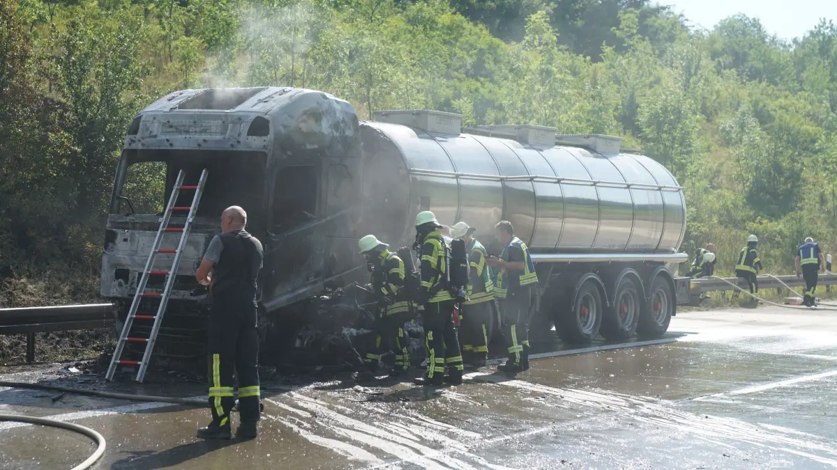 Aichelberg A8: 96 Einsatzkraefte kaempfen gegen Flammeninferno auf der A8 – Tanklastzug brennt vollstaendig aus, Rauchwolke kilometerweit sichtbar: Ein Grossbrand hat am Freitagmorgen fuer einen stundenlangen Feuerwehreinsatz und massive Verkehrsbehinderungen auf der A8 gesorgt. Gegen 9.13 Uhr wurde die Feuerwehr Gruibingen auf die Autobahn zwischen Gruibingen und Aichelberg alarmiert. Dort stand ein Tanklastzug bereits beim Eintreffen der ersten Einsatzkraefte in voller Ausdehnung in Flammen.<br />
<br />
Schon nach wenigen Minuten war klar, dass es sich um einen Grosseinsatz handeln wuerde. Das Feuer hatte bereits auf die angrenzende Boeschung uebergegriffen und breitete sich aufgrund der starken Hitze weiter aus. Aufgrund der dynamischen Einsatzlage wurden umgehend zahlreiche weitere Feuerwehren und Einsatzkraefte nachalarmiert. Die weithin sichtbare Rauchwolke war kilometerweit zu erkennen und sogar im benachbarten Landkreis deutlich sichtbar.<br />
<br />
Insgesamt waren 96 Einsatzkraefte mit 20 Fahrzeugen im Einsatz. Unterstuetzt wurden die Feuerwehren aus dem Landkreis Goeppingen von Kraeften aus dem benachbarten Landkreis Esslingen. Die Zusammenarbeit ueber die Landkreisgrenzen hinweg funktionierte reibungslos und zeigte erneut, wie wichtig die enge Abstimmung der Einsatzkraefte bei Grossschadenslagen ist.<br />
<br />
Der Tanklastzug, eine polnische Zugmaschine, war mit 25.000 Litern Speiseoel beladen. Der Fahrer wurde vorsorglich vom Rettungsdienst untersucht und medizinisch betreut. Nach ersten Erkenntnissen blieb er unverletzt.<br />
<br />
Da zunaechst unklar war, welcher Stoff sich im Tank befand, wurde vorsorglich die Werkfeuerwehr Zeller + Gmelin alarmiert. Damit sollte ausgeschlossen werden, dass sich gefaehrliche Stoffe oder Chemikalien an Bord befinden und bei Bedarf sofort Spezialmassnahmen eingeleitet werden koennen.<br />
<br />
Zur Bekaempfung des Boeschungsbrandes setzte die Feuerwehr Weilheim spezielle Loeschrucksaecke ein. Gleichzeitig wurde ein Pendelverkehr mit Feuerwehrfahrzeugen eingerichtet, um die Einsatzstelle dauerhaft mit Loeschwasser zu versorgen.<br />
<br />
An den umfangreichen Loescharbeiten beteiligt waren die Feuerwehren Gruibingen, Aichelberg, Bad Boll, Bad Ditzenbach, Wiesensteig, Ebersbach, Weilheim an der Teck und Kirchheim unter Teck sowie die Werkfeuerwehr Zeller + Gmelin. Ebenfalls vor Ort waren der Kreisbrandmeister, die Autobahnmeisterei sowie das Forstamt, die den Einsatz unterstuetzten und die notwendigen Massnahmen in ihren jeweiligen Zustaendigkeitsbereichen koordinierten.<br />
<br />
Fuer die umfangreichen Loescharbeiten musste die A8 zeitweise in beide Fahrtrichtungen vollstaendig gesperrt werden. Nachdem der Brand unter Kontrolle gebracht worden war, konnte die Gegenfahrbahn wieder fuer den Verkehr freigegeben werden. In Fahrtrichtung Stuttgart besteht die Sperrung derzeit weiterhin. Dort wird aktuell eine Fahrspur geoeffnet, um den Verkehr langsam abfliessen zu lassen. Zeitweise bildete sich ein Rueckstau von bis zu 15 Kilometern.<br />
<br />
Die hochsommerlichen Temperaturen von rund 34 Grad stellten die Einsatzkraefte zusaetzlich vor enorme Herausforderungen. Besonders Feuerwehrleute unter Atemschutz waren einer extremen koerperlichen Belastung ausgesetzt. Um die im Stau wartenden Verkehrsteilnehmer zu unterstuetzen, verteilte die Feuerwehr Wiesensteig Trinkwasser an die Autofahrer.<br />
<br />
Der ausgebrannte Tanklastzug soll im weiteren Verlauf auf einen Parkplatz gebracht werden. Dort wird die Ladung in ein anderes Fahrzeug umgepumpt, damit die Bergungsarbeiten den Verkehr auf der Autobahn nicht laenger als notwendig beeintraechtigen. Nach derzeitiger Einschaetzung werden die Arbeiten noch mehrere Stunden andauern.<br />
<br />
Wie es zu dem Brand kommen konnte, ist derzeit noch unklar. Die Polizei hat die Ermittlungen zur Brandursache aufgenommen. Auch die Hoehe des entstandenen Sachschadens ist bislang nicht bekannt und wird derzeit ermittelt.<br />
<br />
Bereits am Montag hatte es auf demselben Streckenabschnitt einen groesseren Feuerwehreinsatz mit einem Lastwagen gegeben. Der Brand am Freitag ist damit bereits der zweite groessere Lkw-Grosseinsatz innerhalb einer Woche auf diesem Abschnitt der A8.