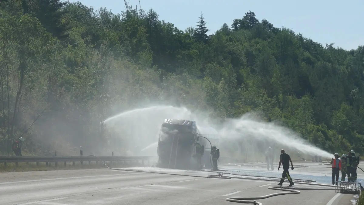 Aichelberg A8: 96 Einsatzkraefte kaempfen gegen Flammeninferno auf der A8 – Tanklastzug brennt vollstaendig aus, Rauchwolke kilometerweit sichtbar: Ein Grossbrand hat am Freitagmorgen fuer einen stundenlangen Feuerwehreinsatz und massive Verkehrsbehinderungen auf der A8 gesorgt. Gegen 9.13 Uhr wurde die Feuerwehr Gruibingen auf die Autobahn zwischen Gruibingen und Aichelberg alarmiert. Dort stand ein Tanklastzug bereits beim Eintreffen der ersten Einsatzkraefte in voller Ausdehnung in Flammen.<br />
<br />
Schon nach wenigen Minuten war klar, dass es sich um einen Grosseinsatz handeln wuerde. Das Feuer hatte bereits auf die angrenzende Boeschung uebergegriffen und breitete sich aufgrund der starken Hitze weiter aus. Aufgrund der dynamischen Einsatzlage wurden umgehend zahlreiche weitere Feuerwehren und Einsatzkraefte nachalarmiert. Die weithin sichtbare Rauchwolke war kilometerweit zu erkennen und sogar im benachbarten Landkreis deutlich sichtbar.<br />
<br />
Insgesamt waren 96 Einsatzkraefte mit 20 Fahrzeugen im Einsatz. Unterstuetzt wurden die Feuerwehren aus dem Landkreis Goeppingen von Kraeften aus dem benachbarten Landkreis Esslingen. Die Zusammenarbeit ueber die Landkreisgrenzen hinweg funktionierte reibungslos und zeigte erneut, wie wichtig die enge Abstimmung der Einsatzkraefte bei Grossschadenslagen ist.<br />
<br />
Der Tanklastzug, eine polnische Zugmaschine, war mit 25.000 Litern Speiseoel beladen. Der Fahrer wurde vorsorglich vom Rettungsdienst untersucht und medizinisch betreut. Nach ersten Erkenntnissen blieb er unverletzt.<br />
<br />
Da zunaechst unklar war, welcher Stoff sich im Tank befand, wurde vorsorglich die Werkfeuerwehr Zeller + Gmelin alarmiert. Damit sollte ausgeschlossen werden, dass sich gefaehrliche Stoffe oder Chemikalien an Bord befinden und bei Bedarf sofort Spezialmassnahmen eingeleitet werden koennen.<br />
<br />
Zur Bekaempfung des Boeschungsbrandes setzte die Feuerwehr Weilheim spezielle Loeschrucksaecke ein. Gleichzeitig wurde ein Pendelverkehr mit Feuerwehrfahrzeugen eingerichtet, um die Einsatzstelle dauerhaft mit Loeschwasser zu versorgen.<br />
<br />
An den umfangreichen Loescharbeiten beteiligt waren die Feuerwehren Gruibingen, Aichelberg, Bad Boll, Bad Ditzenbach, Wiesensteig, Ebersbach, Weilheim an der Teck und Kirchheim unter Teck sowie die Werkfeuerwehr Zeller + Gmelin. Ebenfalls vor Ort waren der Kreisbrandmeister, die Autobahnmeisterei sowie das Forstamt, die den Einsatz unterstuetzten und die notwendigen Massnahmen in ihren jeweiligen Zustaendigkeitsbereichen koordinierten.<br />
<br />
Fuer die umfangreichen Loescharbeiten musste die A8 zeitweise in beide Fahrtrichtungen vollstaendig gesperrt werden. Nachdem der Brand unter Kontrolle gebracht worden war, konnte die Gegenfahrbahn wieder fuer den Verkehr freigegeben werden. In Fahrtrichtung Stuttgart besteht die Sperrung derzeit weiterhin. Dort wird aktuell eine Fahrspur geoeffnet, um den Verkehr langsam abfliessen zu lassen. Zeitweise bildete sich ein Rueckstau von bis zu 15 Kilometern.<br />
<br />
Die hochsommerlichen Temperaturen von rund 34 Grad stellten die Einsatzkraefte zusaetzlich vor enorme Herausforderungen. Besonders Feuerwehrleute unter Atemschutz waren einer extremen koerperlichen Belastung ausgesetzt. Um die im Stau wartenden Verkehrsteilnehmer zu unterstuetzen, verteilte die Feuerwehr Wiesensteig Trinkwasser an die Autofahrer.<br />
<br />
Der ausgebrannte Tanklastzug soll im weiteren Verlauf auf einen Parkplatz gebracht werden. Dort wird die Ladung in ein anderes Fahrzeug umgepumpt, damit die Bergungsarbeiten den Verkehr auf der Autobahn nicht laenger als notwendig beeintraechtigen. Nach derzeitiger Einschaetzung werden die Arbeiten noch mehrere Stunden andauern.<br />
<br />
Wie es zu dem Brand kommen konnte, ist derzeit noch unklar. Die Polizei hat die Ermittlungen zur Brandursache aufgenommen. Auch die Hoehe des entstandenen Sachschadens ist bislang nicht bekannt und wird derzeit ermittelt.<br />
<br />
Bereits am Montag hatte es auf demselben Streckenabschnitt einen groesseren Feuerwehreinsatz mit einem Lastwagen gegeben. Der Brand am Freitag ist damit bereits der zweite groessere Lkw-Grosseinsatz innerhalb einer Woche auf diesem Abschnitt der A8.