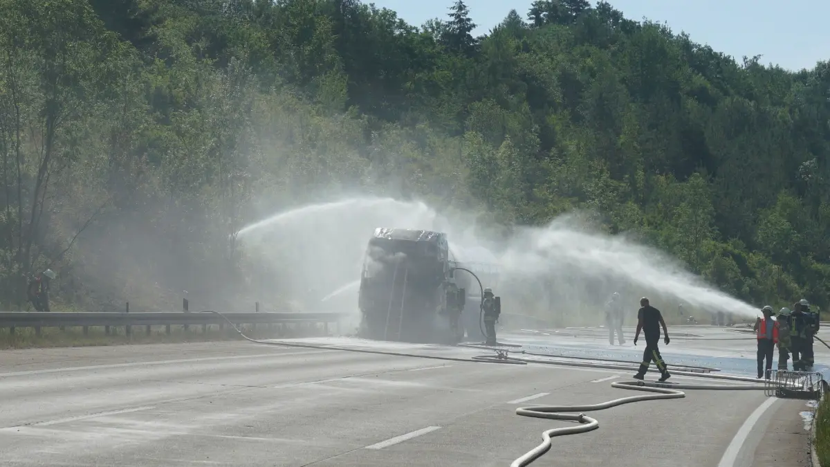Aichelberg A8: 96 Einsatzkraefte kaempfen gegen Flammeninferno auf der A8 – Tanklastzug brennt vollstaendig aus, Rauchwolke kilometerweit sichtbar: Ein Grossbrand hat am Freitagmorgen fuer einen stundenlangen Feuerwehreinsatz und massive Verkehrsbehinderungen auf der A8 gesorgt. Gegen 9.13 Uhr wurde die Feuerwehr Gruibingen auf die Autobahn zwischen Gruibingen und Aichelberg alarmiert. Dort stand ein Tanklastzug bereits beim Eintreffen der ersten Einsatzkraefte in voller Ausdehnung in Flammen.<br />
<br />
Schon nach wenigen Minuten war klar, dass es sich um einen Grosseinsatz handeln wuerde. Das Feuer hatte bereits auf die angrenzende Boeschung uebergegriffen und breitete sich aufgrund der starken Hitze weiter aus. Aufgrund der dynamischen Einsatzlage wurden umgehend zahlreiche weitere Feuerwehren und Einsatzkraefte nachalarmiert. Die weithin sichtbare Rauchwolke war kilometerweit zu erkennen und sogar im benachbarten Landkreis deutlich sichtbar.<br />
<br />
Insgesamt waren 96 Einsatzkraefte mit 20 Fahrzeugen im Einsatz. Unterstuetzt wurden die Feuerwehren aus dem Landkreis Goeppingen von Kraeften aus dem benachbarten Landkreis Esslingen. Die Zusammenarbeit ueber die Landkreisgrenzen hinweg funktionierte reibungslos und zeigte erneut, wie wichtig die enge Abstimmung der Einsatzkraefte bei Grossschadenslagen ist.<br />
<br />
Der Tanklastzug, eine polnische Zugmaschine, war mit 25.000 Litern Speiseoel beladen. Der Fahrer wurde vorsorglich vom Rettungsdienst untersucht und medizinisch betreut. Nach ersten Erkenntnissen blieb er unverletzt.<br />
<br />
Da zunaechst unklar war, welcher Stoff sich im Tank befand, wurde vorsorglich die Werkfeuerwehr Zeller + Gmelin alarmiert. Damit sollte ausgeschlossen werden, dass sich gefaehrliche Stoffe oder Chemikalien an Bord befinden und bei Bedarf sofort Spezialmassnahmen eingeleitet werden koennen.<br />
<br />
Zur Bekaempfung des Boeschungsbrandes setzte die Feuerwehr Weilheim spezielle Loeschrucksaecke ein. Gleichzeitig wurde ein Pendelverkehr mit Feuerwehrfahrzeugen eingerichtet, um die Einsatzstelle dauerhaft mit Loeschwasser zu versorgen.<br />
<br />
An den umfangreichen Loescharbeiten beteiligt waren die Feuerwehren Gruibingen, Aichelberg, Bad Boll, Bad Ditzenbach, Wiesensteig, Ebersbach, Weilheim an der Teck und Kirchheim unter Teck sowie die Werkfeuerwehr Zeller + Gmelin. Ebenfalls vor Ort waren der Kreisbrandmeister, die Autobahnmeisterei sowie das Forstamt, die den Einsatz unterstuetzten und die notwendigen Massnahmen in ihren jeweiligen Zustaendigkeitsbereichen koordinierten.<br />
<br />
Fuer die umfangreichen Loescharbeiten musste die A8 zeitweise in beide Fahrtrichtungen vollstaendig gesperrt werden. Nachdem der Brand unter Kontrolle gebracht worden war, konnte die Gegenfahrbahn wieder fuer den Verkehr freigegeben werden. In Fahrtrichtung Stuttgart besteht die Sperrung derzeit weiterhin. Dort wird aktuell eine Fahrspur geoeffnet, um den Verkehr langsam abfliessen zu lassen. Zeitweise bildete sich ein Rueckstau von bis zu 15 Kilometern.<br />
<br />
Die hochsommerlichen Temperaturen von rund 34 Grad stellten die Einsatzkraefte zusaetzlich vor enorme Herausforderungen. Besonders Feuerwehrleute unter Atemschutz waren einer extremen koerperlichen Belastung ausgesetzt. Um die im Stau wartenden Verkehrsteilnehmer zu unterstuetzen, verteilte die Feuerwehr Wiesensteig Trinkwasser an die Autofahrer.<br />
<br />
Der ausgebrannte Tanklastzug soll im weiteren Verlauf auf einen Parkplatz gebracht werden. Dort wird die Ladung in ein anderes Fahrzeug umgepumpt, damit die Bergungsarbeiten den Verkehr auf der Autobahn nicht laenger als notwendig beeintraechtigen. Nach derzeitiger Einschaetzung werden die Arbeiten noch mehrere Stunden andauern.<br />
<br />
Wie es zu dem Brand kommen konnte, ist derzeit noch unklar. Die Polizei hat die Ermittlungen zur Brandursache aufgenommen. Auch die Hoehe des entstandenen Sachschadens ist bislang nicht bekannt und wird derzeit ermittelt.<br />
<br />
Bereits am Montag hatte es auf demselben Streckenabschnitt einen groesseren Feuerwehreinsatz mit einem Lastwagen gegeben. Der Brand am Freitag ist damit bereits der zweite groessere Lkw-Grosseinsatz innerhalb einer Woche auf diesem Abschnitt der A8.